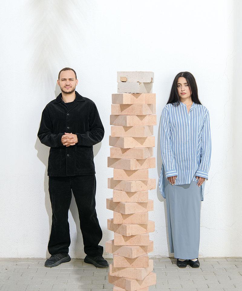 Khaled & Sara pictured standing, with a tall stack of Datecrete tiles between them.